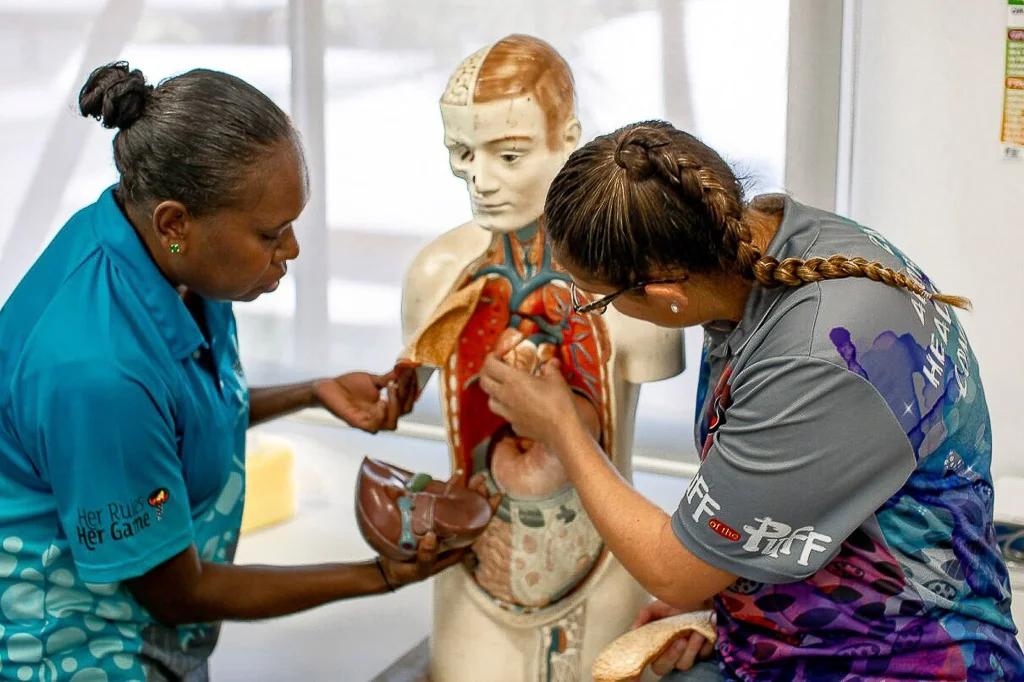 Two Aboriginal health workers examine an anatomical torso model during a medical training session.
